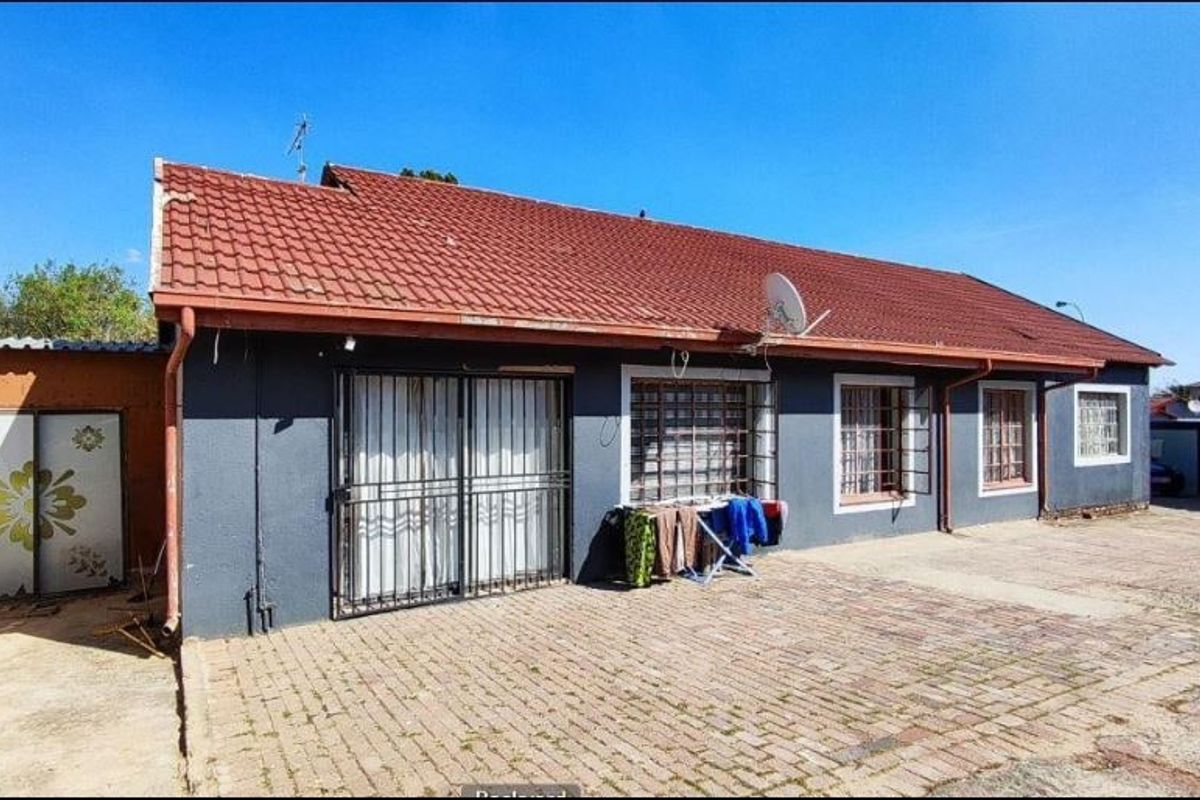 Rear exterior view of the house featuring a terracotta tiled roof, paved courtyard area, and security bars on windows and sliding doors.