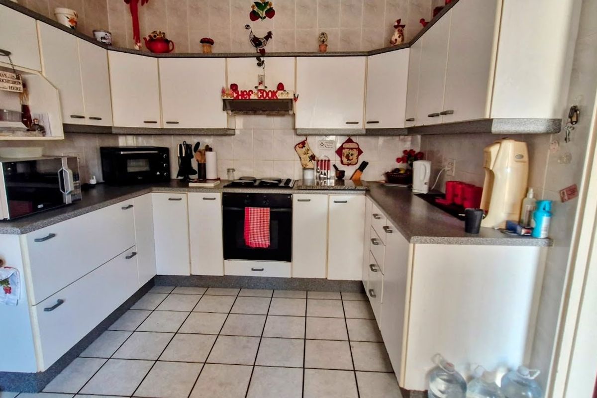 A functional U-shaped kitchen featuring white cabinetry, laminate countertops, built-in oven, hob, extractor fan, and tiled flooring.