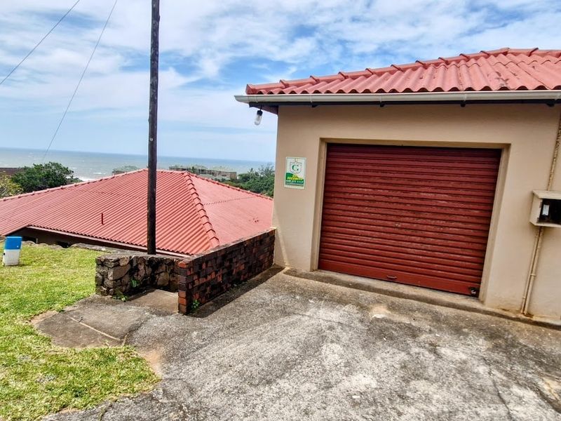 Exterior view of a double garage with roller doors, featuring a concrete driveway and scenic coastal views in the background.