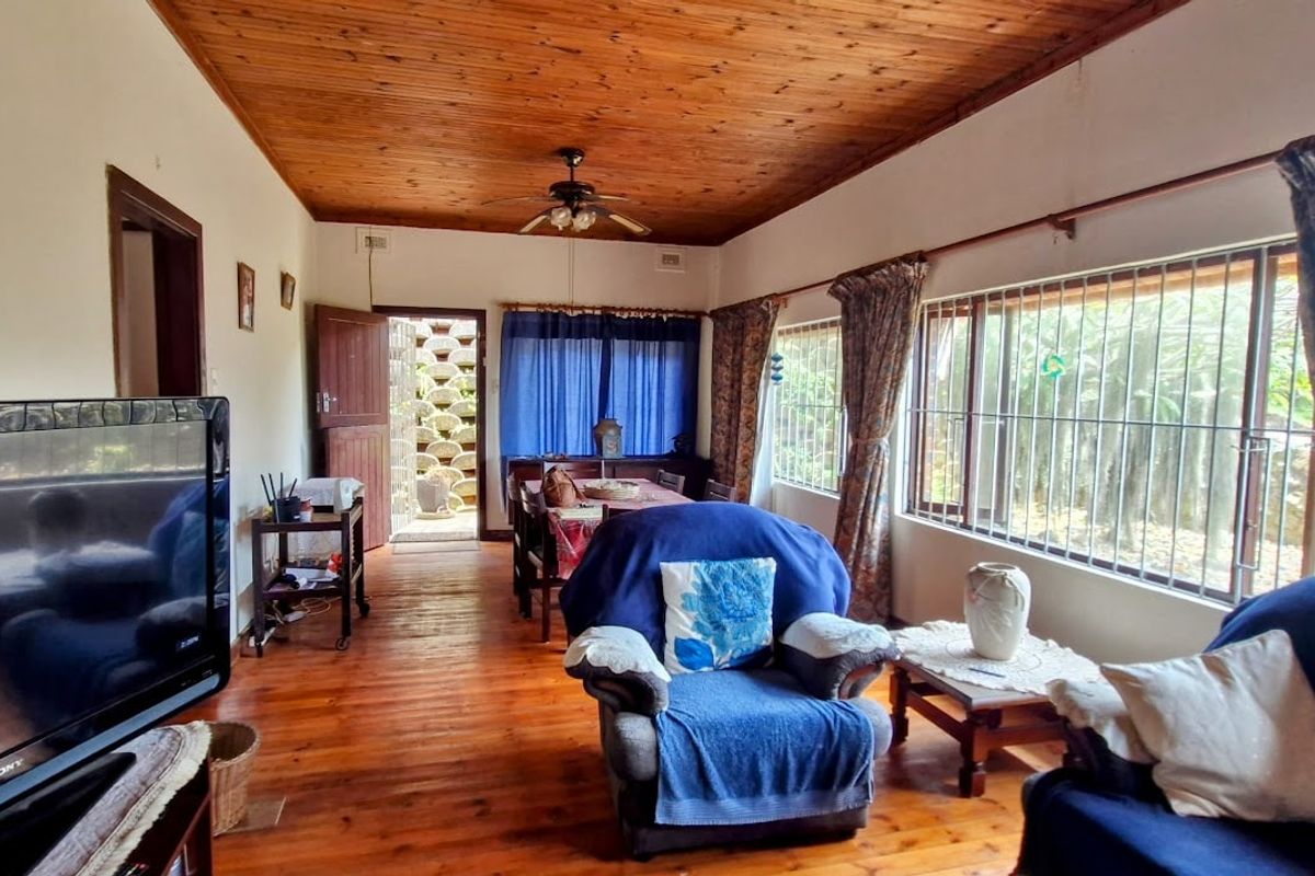 A living room featuring warm timber ceilings and flooring, with large windows fitted with security bars and direct access to an outdoor area.