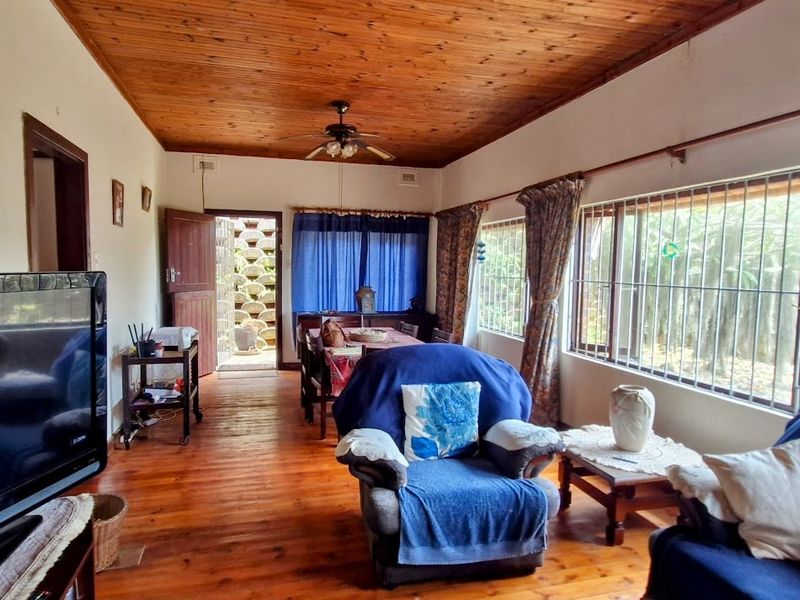 A living room featuring warm timber ceilings and flooring, with large windows fitted with security bars and direct access to an outdoor area.