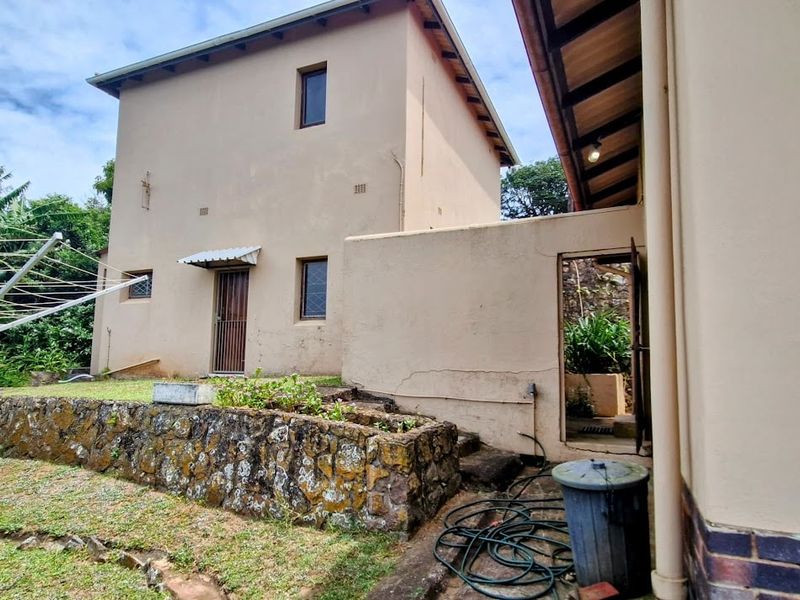 Rear view of the property featuring a stone retaining wall, plastered exterior facade, and access to the garden area.