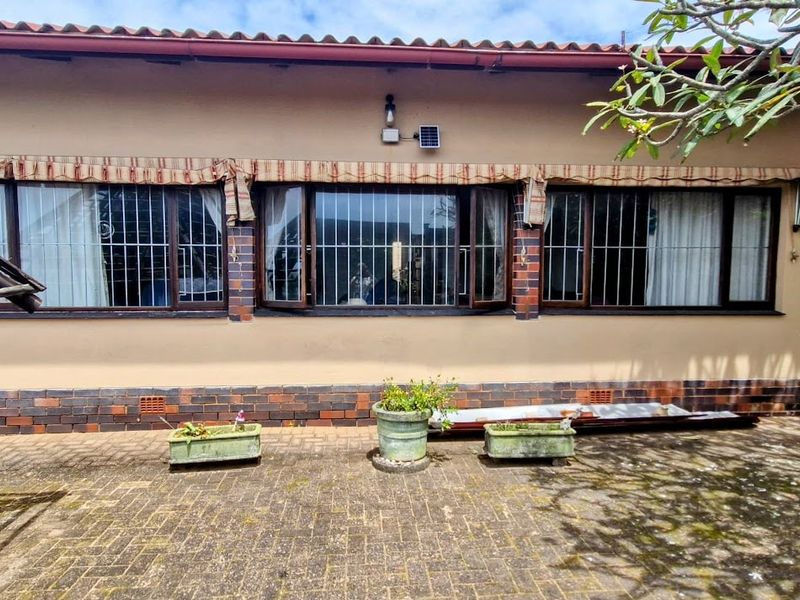 Rear exterior view of the house featuring brick paving, a tiled roof, and security bars on the windows.