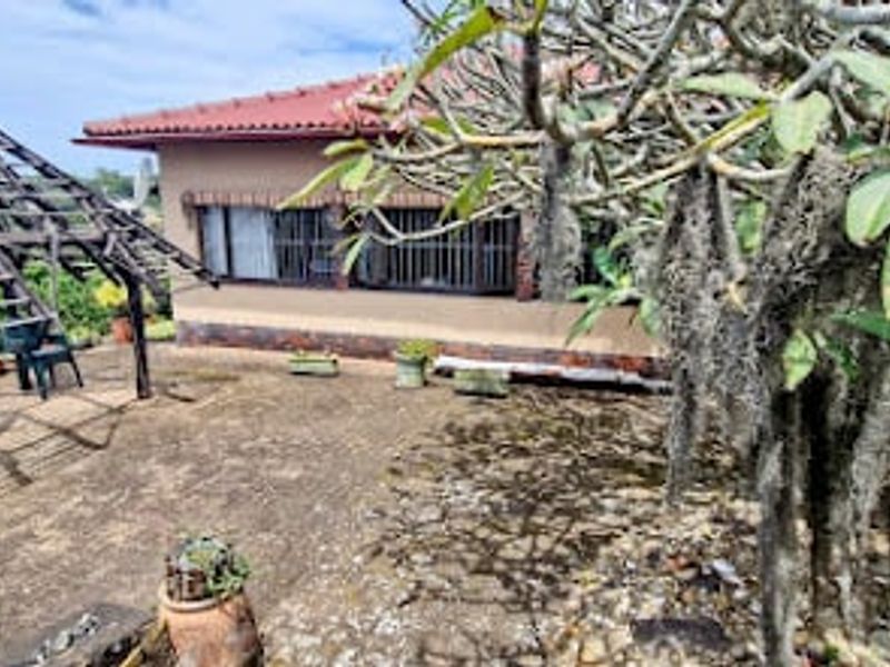 Rear exterior view featuring a paved patio area, a wooden pergola structure, and a brick house facade with security bars on the windows.