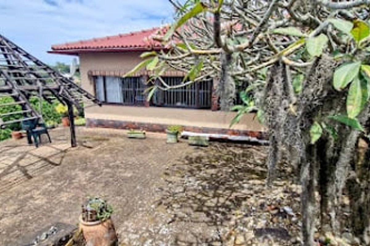 Rear exterior view featuring a paved patio area, a wooden pergola structure, and a brick house facade with security bars on the windows.