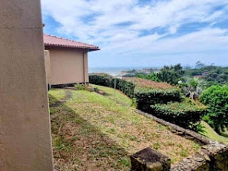 Rear exterior view of the property featuring a landscaped garden, retaining wall, and distant coastal views.