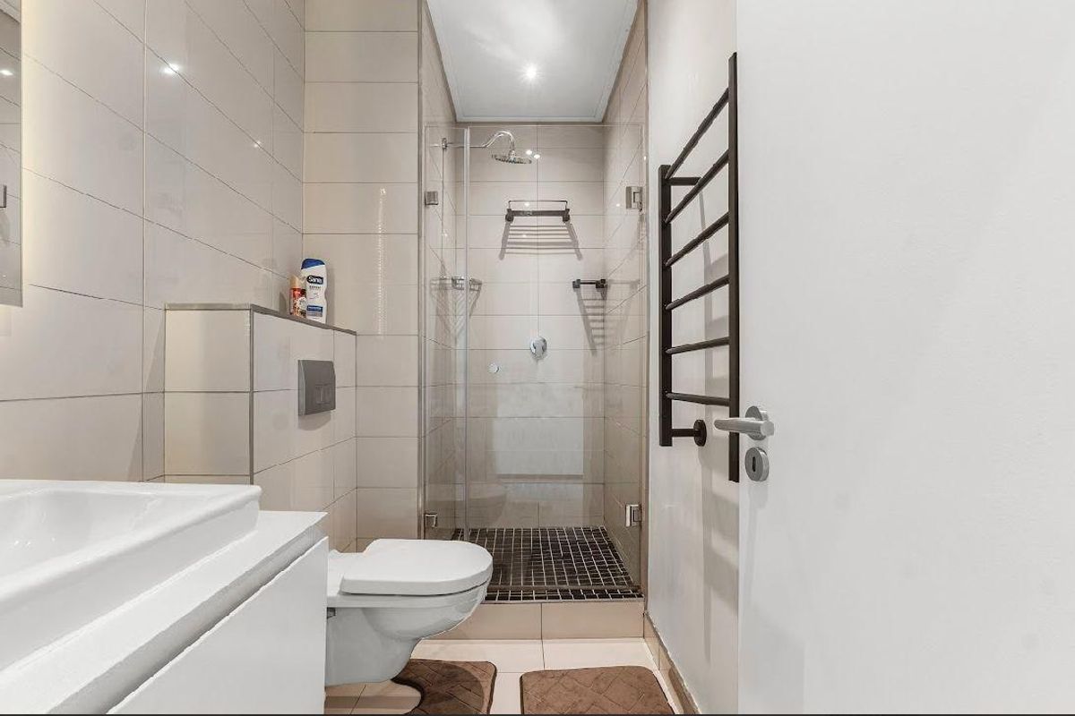 Modern bathroom featuring a glass-enclosed shower, wall-mounted toilet, vanity basin, and a sleek black heated towel rail with neutral wall tiling.