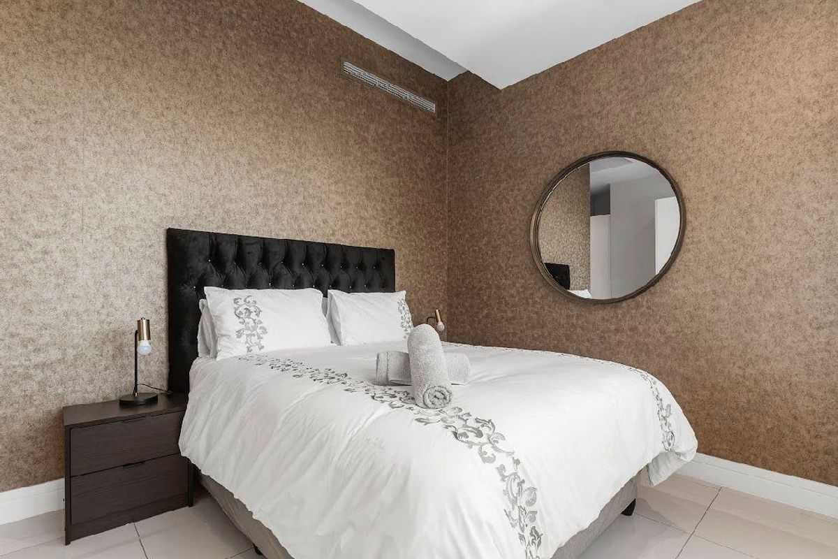 A well-maintained bedroom featuring neutral textured wallpaper, tiled flooring, and integrated ceiling air conditioning vents.