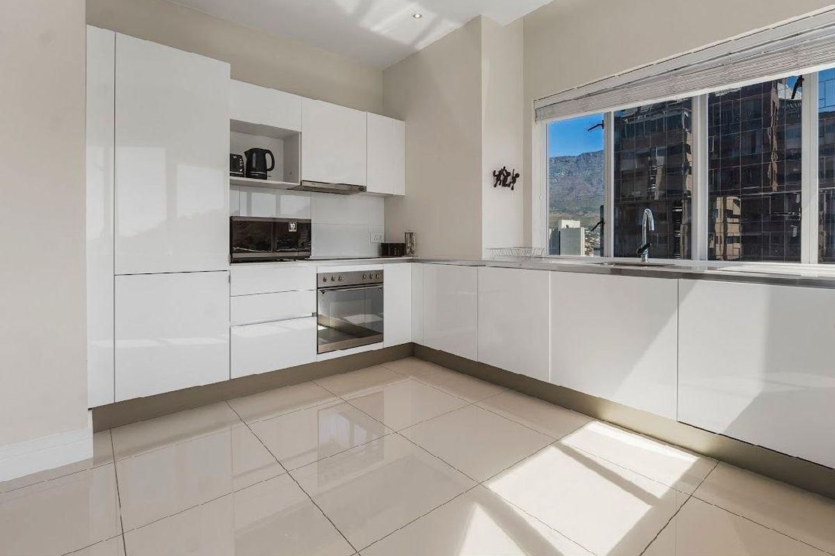 Modern kitchen featuring sleek white cabinetry, built-in appliances, tiled flooring, and large windows offering natural light and urban views.