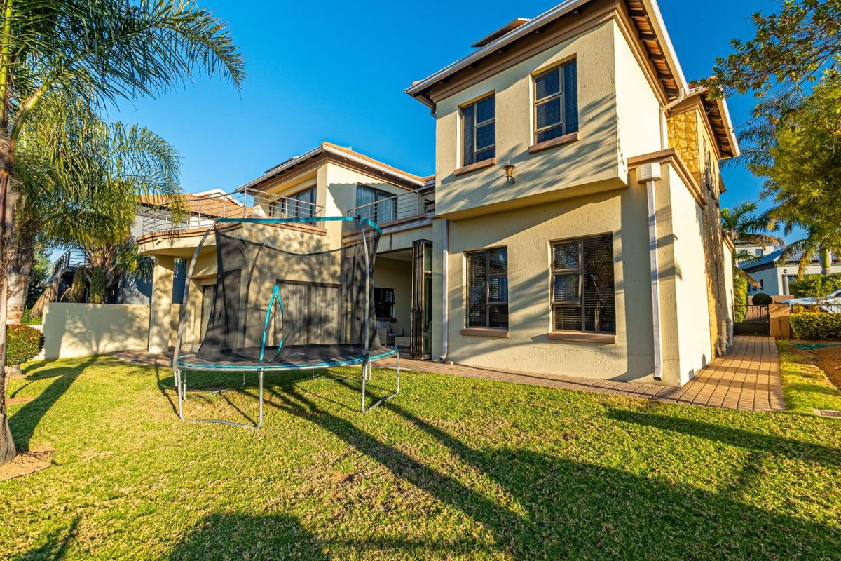 Rear view of a two-story residential property featuring a paved patio, balcony, and well-maintained garden area.