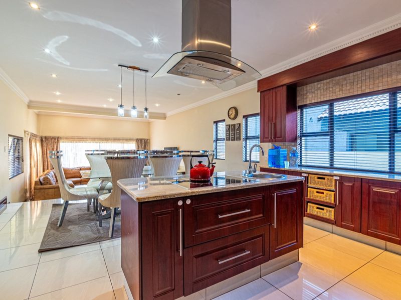 Spacious open-plan kitchen and dining area featuring dark wood cabinetry, granite countertops, a central island with a hob, and modern recessed lighting.
