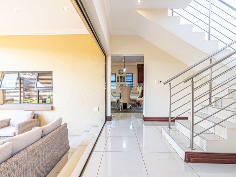 Open plan living area featuring polished tiled floors, a modern staircase with stainless steel balustrades, and seamless access to the outdoor patio area.
