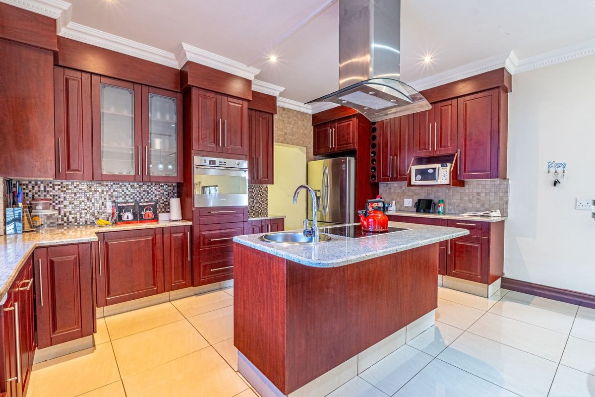 A well-appointed kitchen featuring rich cherry wood cabinetry, granite countertops, a central island, and a stainless steel extractor fan with mosaic tile backsplash.