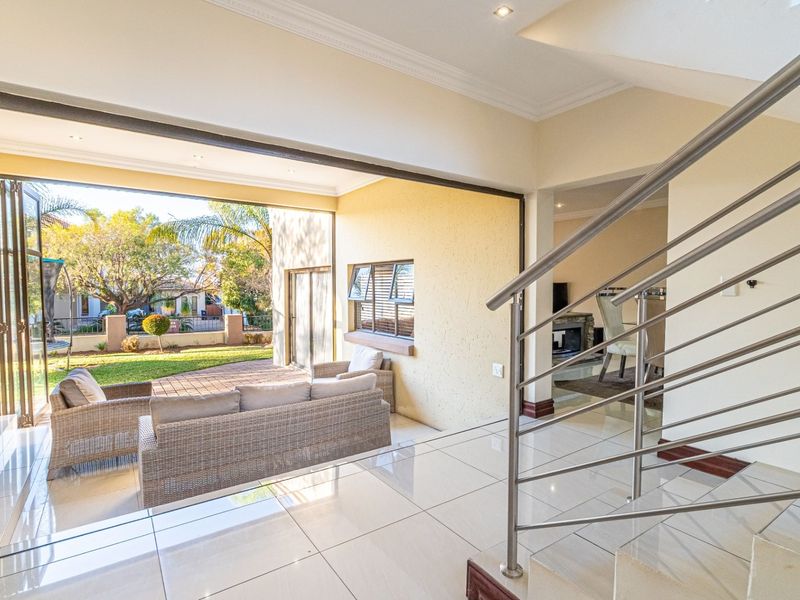 Spacious open-plan living area featuring polished tiled floors, modern stainless steel staircase railing, and large bi-fold doors opening onto a patio and garden.
