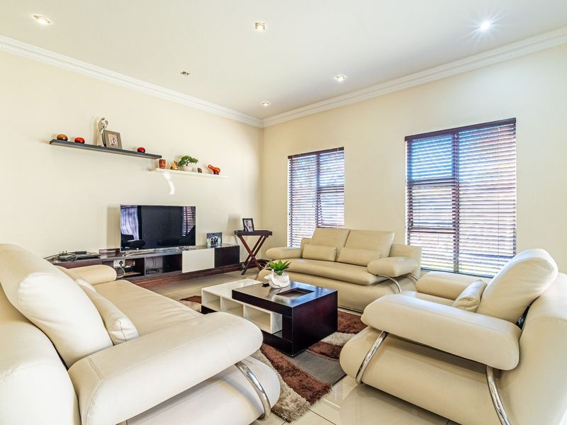 A well-maintained living room featuring tiled flooring, recessed downlighting, crown molding, and venetian blinds, creating a bright and comfortable space.