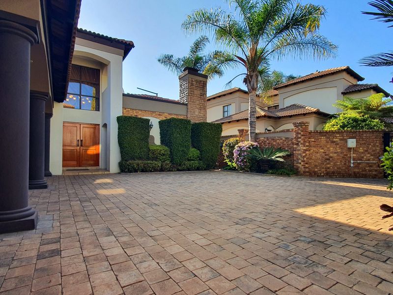 A well-maintained front entrance featuring a paved driveway, double wooden doors, and a stone chimney, set within a landscaped residential property.
