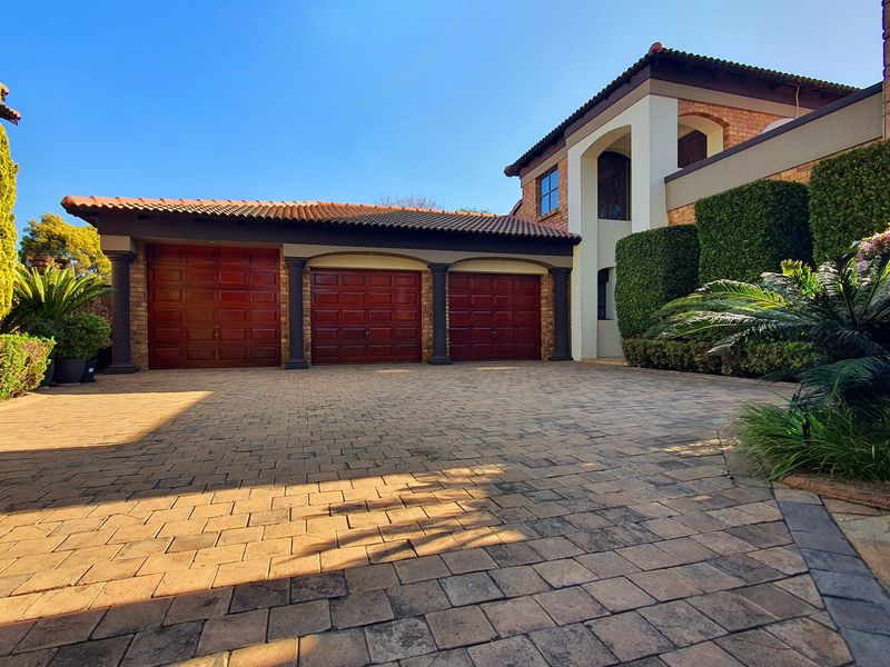 A well-maintained front exterior featuring a triple garage with wooden doors, a spacious paved driveway, and established garden hedges.