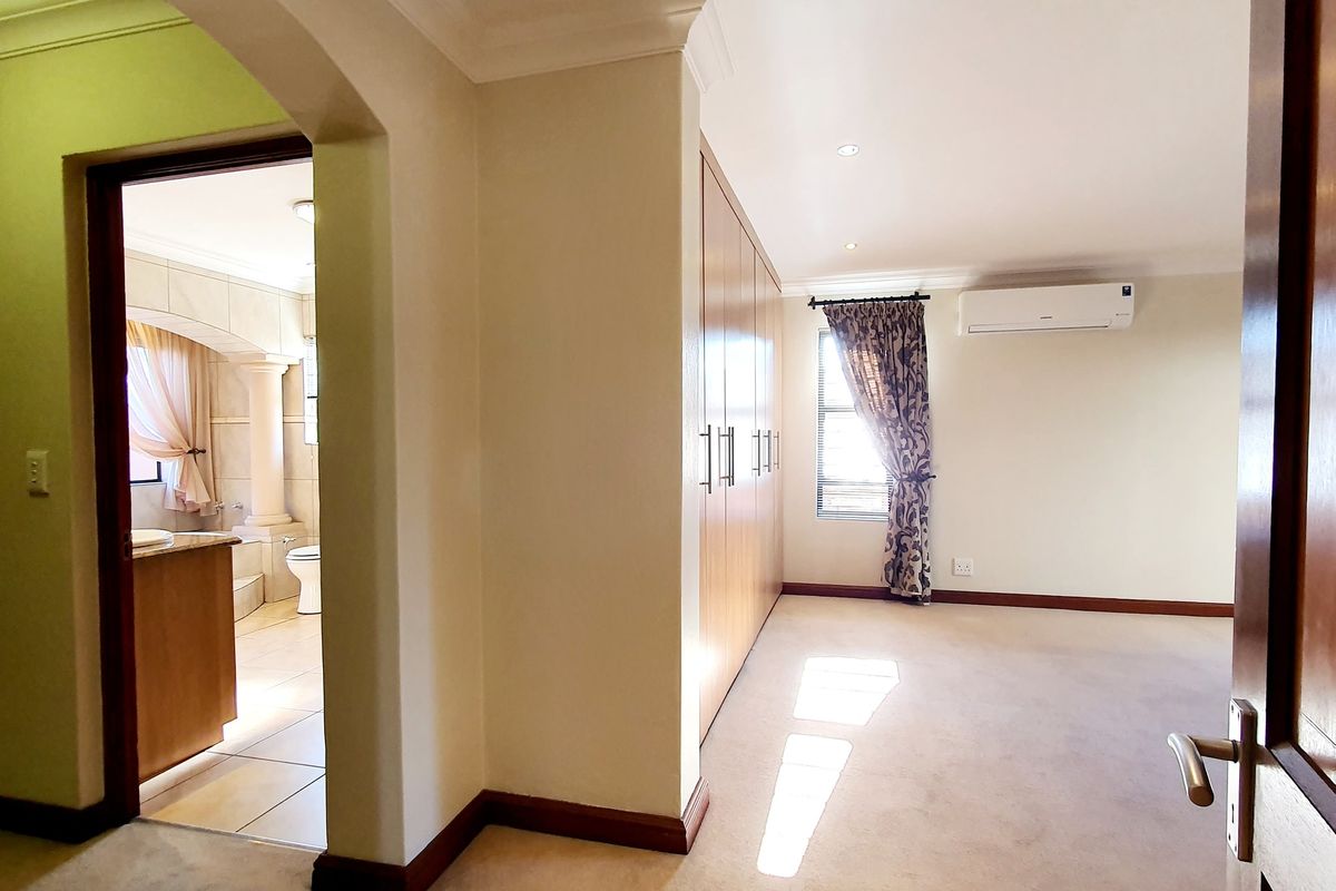 Spacious bedroom featuring built-in cupboards, air conditioning, and an adjoining en-suite bathroom, presented in a clean, neutral finish.