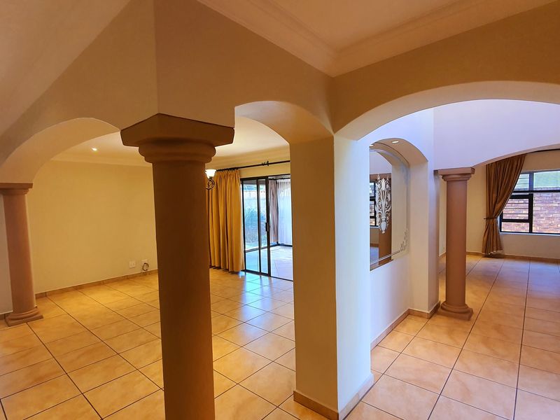 Spacious open-plan living area featuring decorative columns, arched architectural details, ceramic tiled flooring, and large sliding doors leading to the exterior.