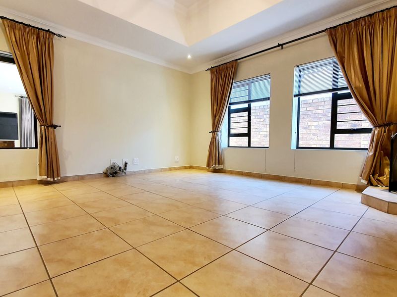 Spacious living room featuring a tray ceiling, large windows with natural light, and neutral tiled flooring.