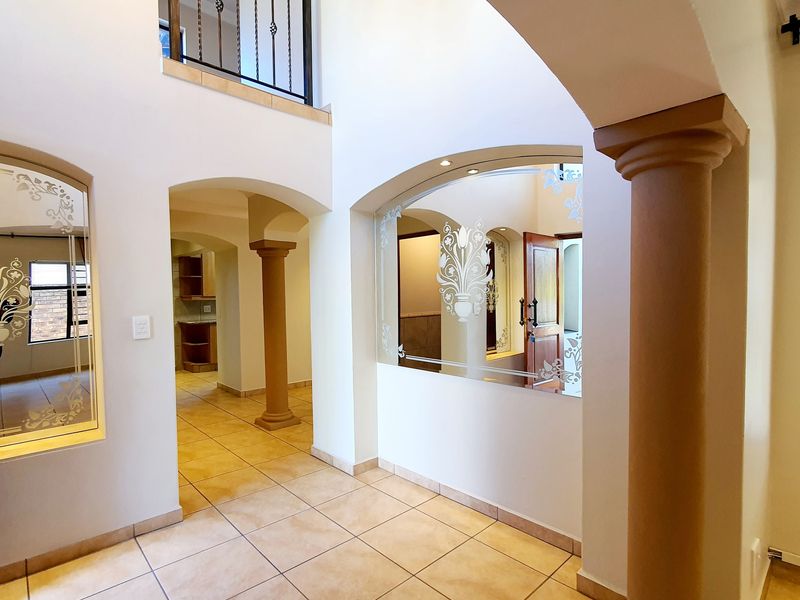 Spacious double-volume entrance hall featuring tiled flooring, decorative columns, arched architectural details, and a mezzanine balcony with a wrought iron balustrade.