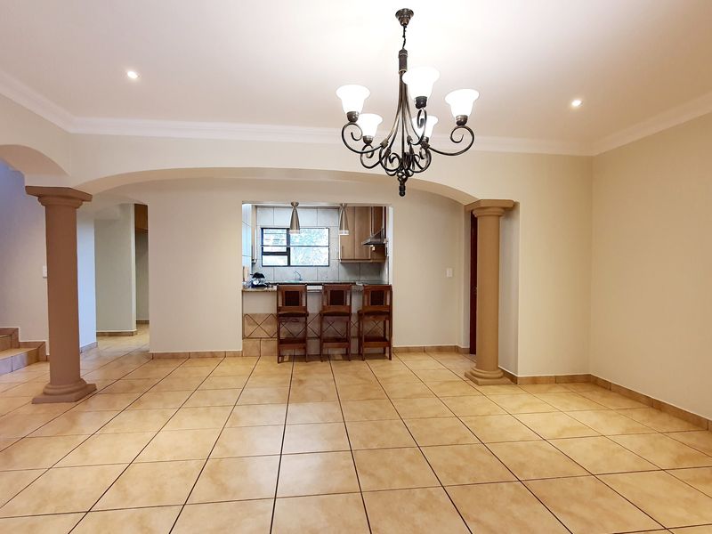 Spacious open-plan living area featuring ceramic floor tiles, decorative columns, and an arched transition to a functional kitchen with a breakfast bar.