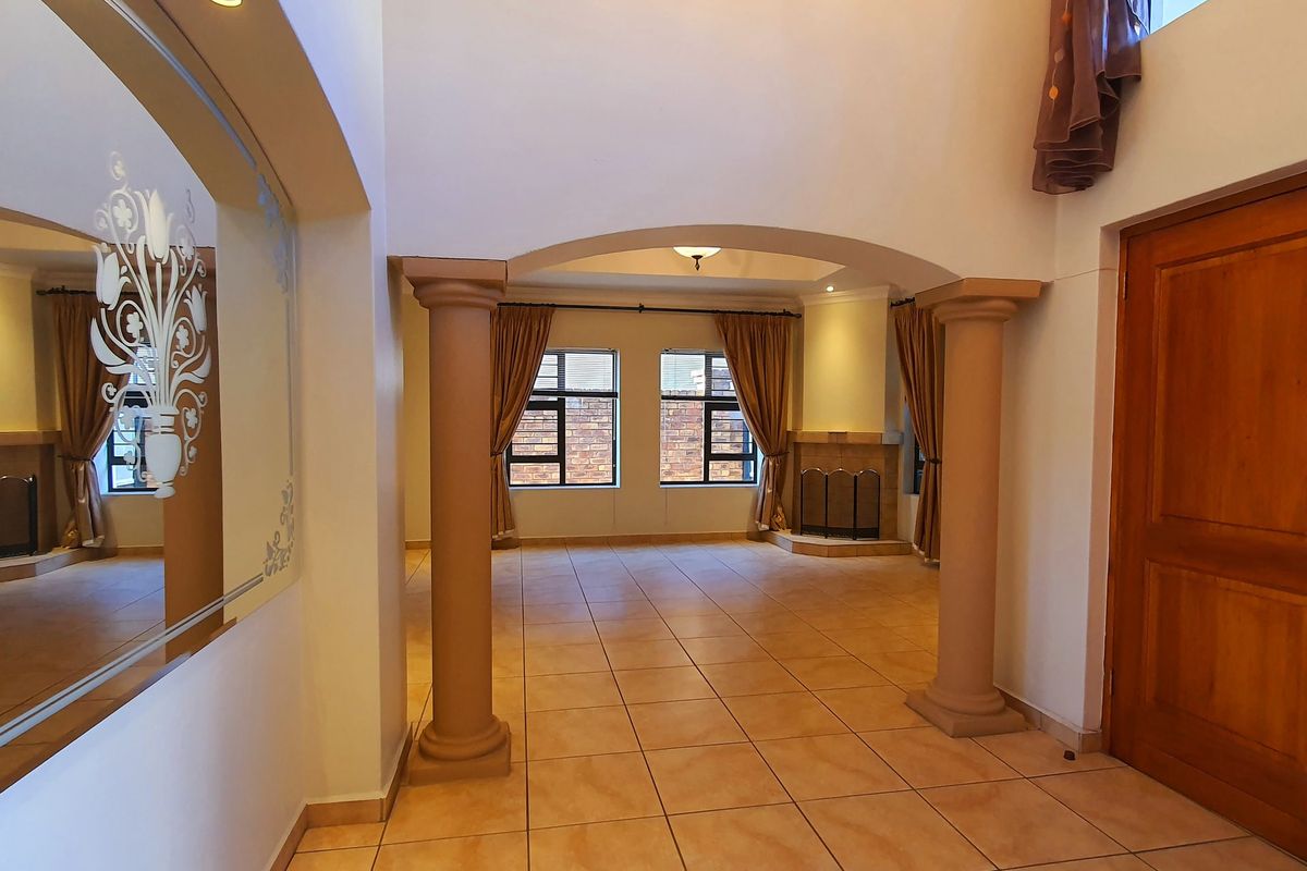 Spacious living area featuring tiled flooring, decorative columns, an elegant archway, and a built-in fireplace, offering a bright and open layout.