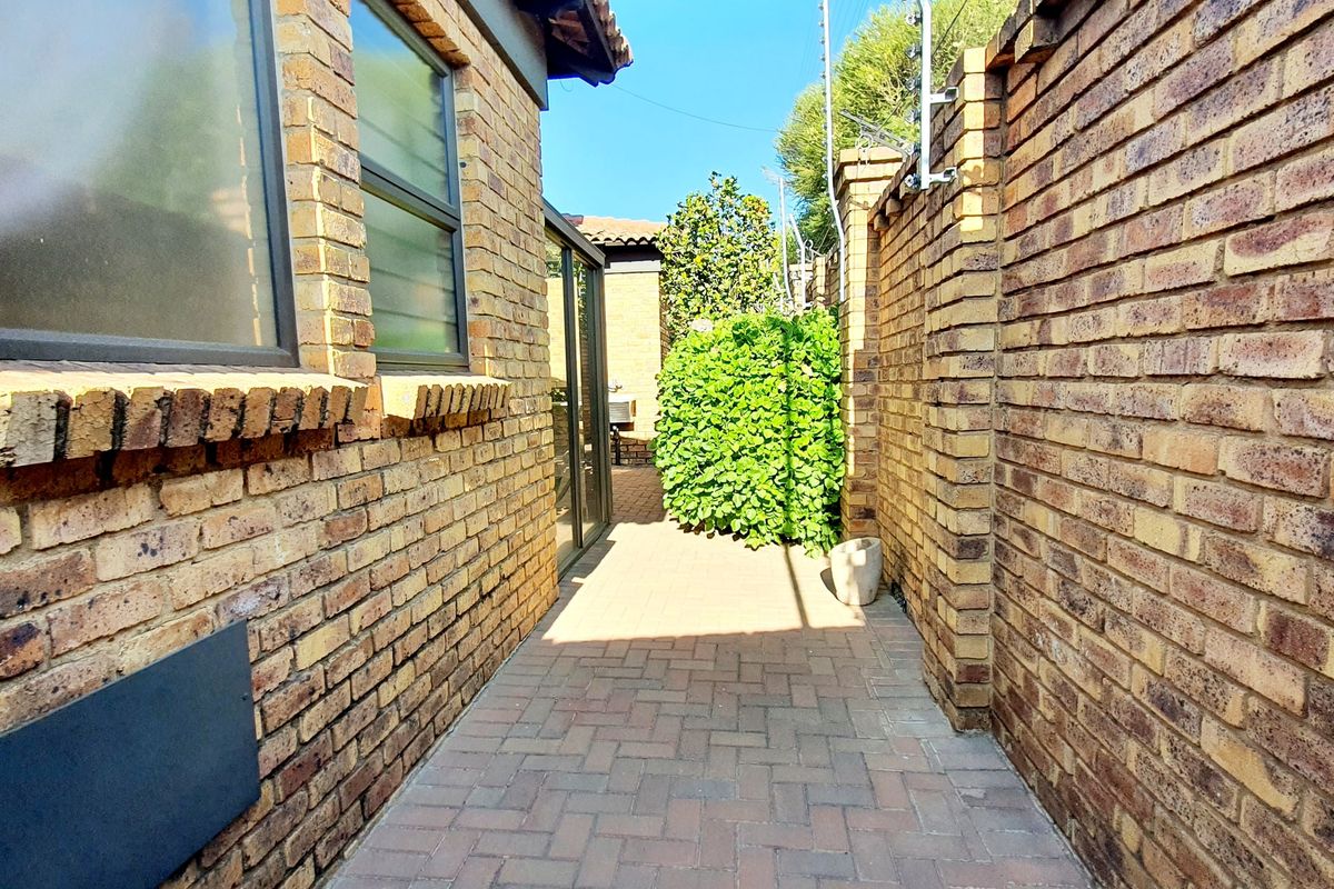 A side walkway featuring face brick walls, paved flooring, and secure electric fencing along the perimeter.