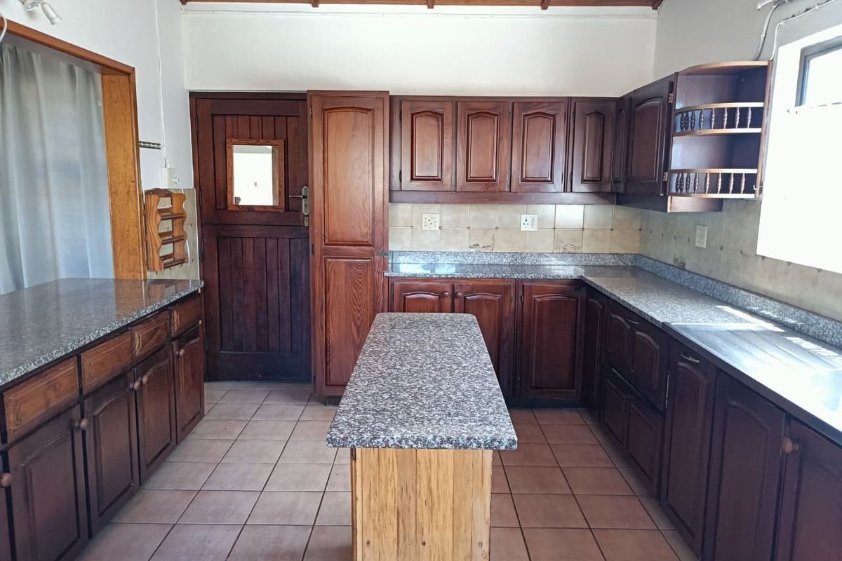 A functional kitchen featuring dark wood cabinetry, granite countertops, a central island, and tiled flooring with a timber-paneled ceiling.