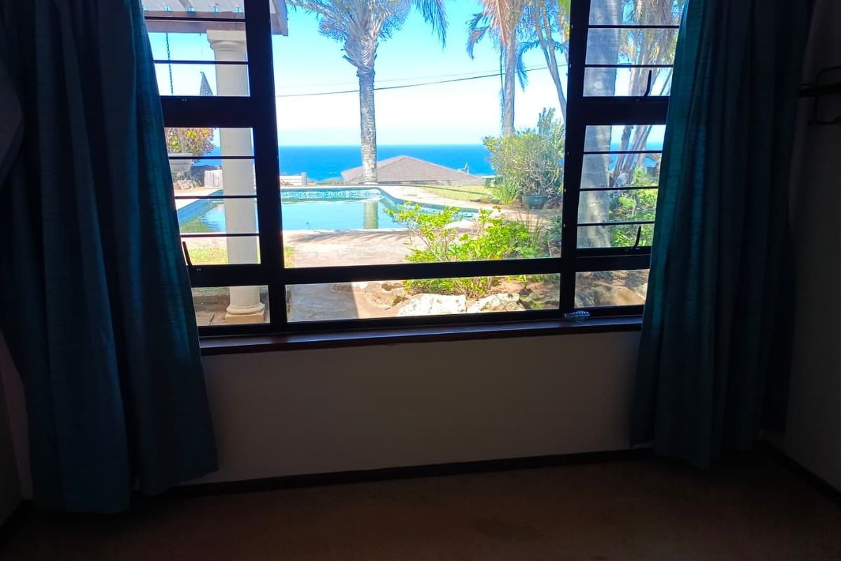A bedroom featuring a large window with security bars, offering a scenic view of the swimming pool and ocean beyond.