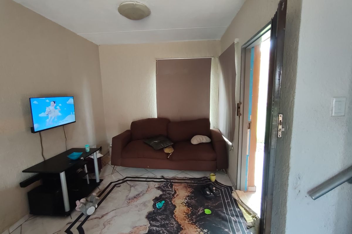 A compact living room featuring tiled flooring and roller blinds, providing direct access to the exterior through a security gate.