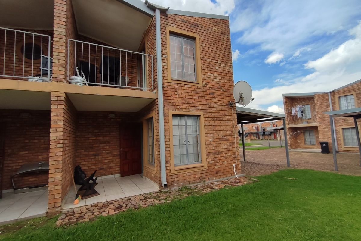 Rear view of a face brick townhouse featuring a ground floor tiled patio and an upper-level balcony with metal railings.