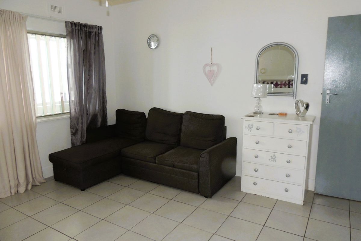 A living room featuring neutral ceramic floor tiles, a window with security bars, and a standard interior door.