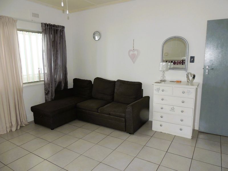 A living room featuring neutral ceramic floor tiles, a window with security bars, and a standard interior door.