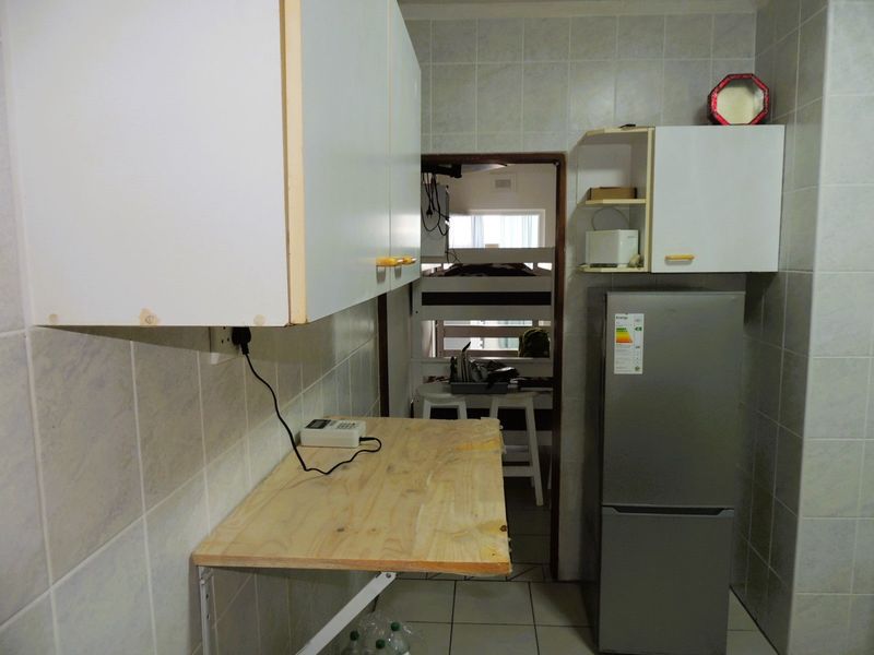 A compact kitchen area featuring tiled walls, wall-mounted cabinetry, and a fold-down wooden counter, showing signs of wear and dated finishes.