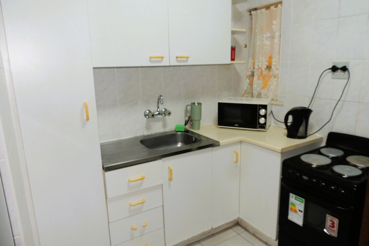 A compact kitchen featuring white cabinetry, laminate countertops, a stainless steel sink, and tiled finishes, offering a functional space ready for modernization.