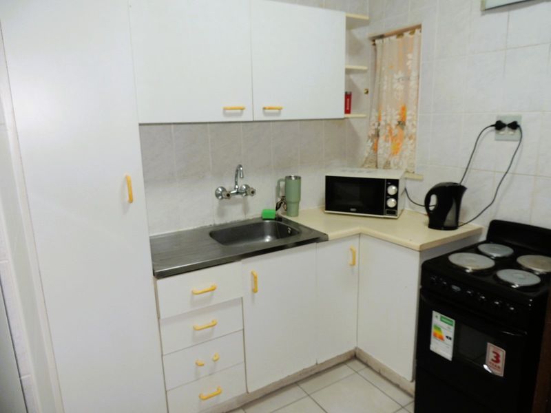 A compact kitchen featuring white cabinetry, laminate countertops, a stainless steel sink, and tiled finishes, offering a functional space ready for modernization.