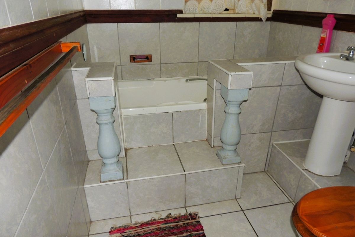 A dated bathroom featuring a built-in tiled bathtub with decorative columns, a pedestal basin, and full-height wall tiling.