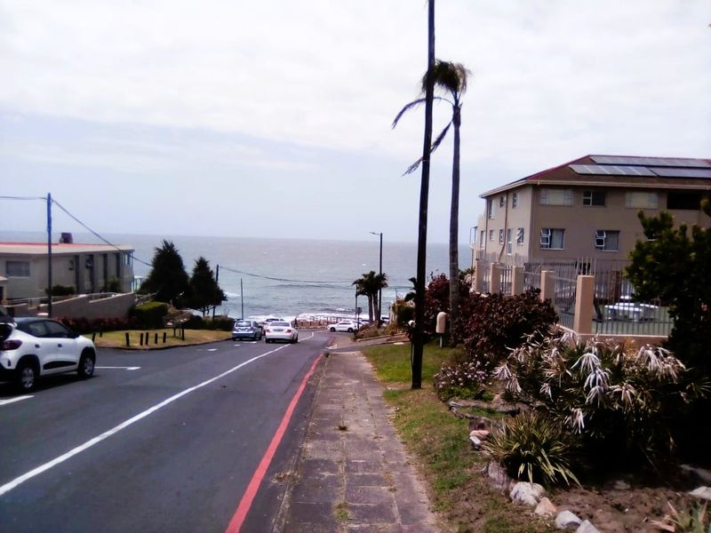 A street-level view of the coastal apartment complex, showing the road, sidewalk, and proximity to the ocean.