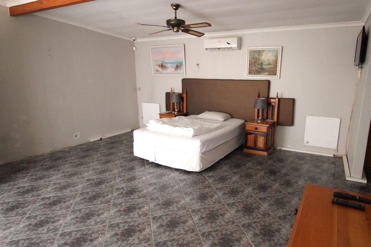 Spacious bedroom featuring tiled flooring, a ceiling fan, and a wall-mounted air conditioning unit.