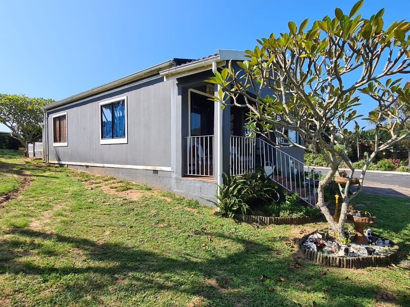 Exterior view of a detached townhouse featuring grey cladding, a covered front porch with metal railing, and a surrounding lawn area.