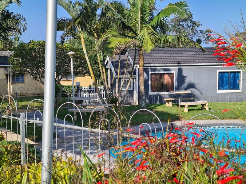 A view of a townhouse complex pool area featuring a swimming pool, paved walkways, and well-maintained garden surroundings.