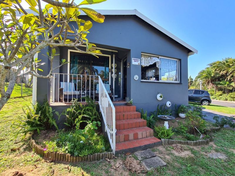 Front elevation of a townhouse featuring a covered porch, tiled entrance steps with metal railing, and established garden landscaping.