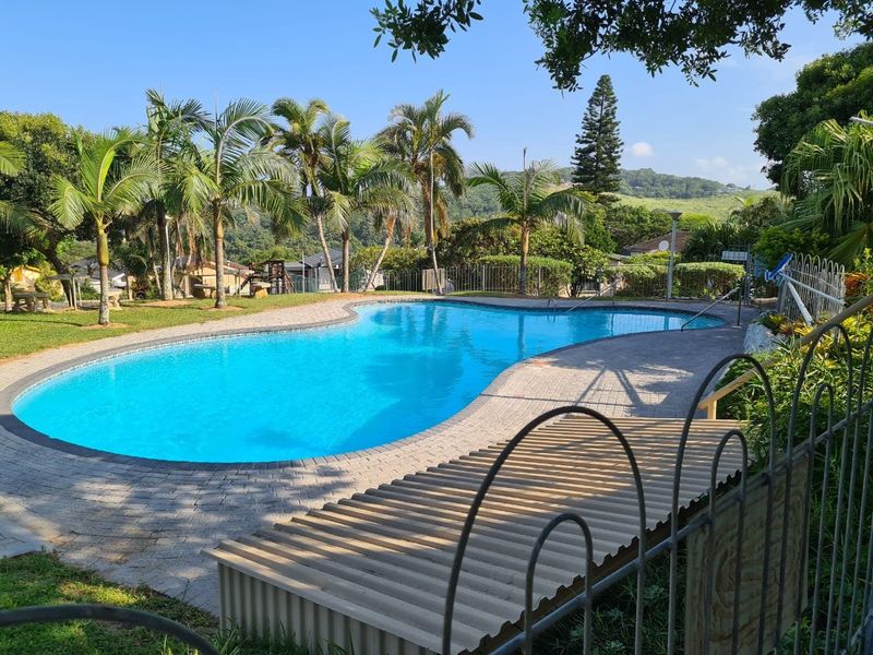 A well-maintained outdoor swimming pool area featuring paved surrounds, lush landscaping, and secure perimeter fencing in a tranquil setting.