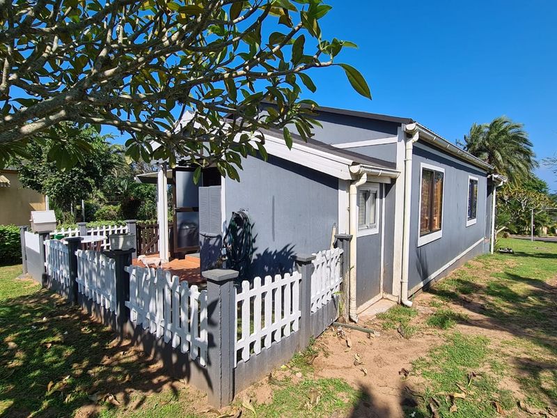 Rear view of the townhouse featuring a small tiled patio area enclosed by a white picket fence and established garden surroundings.