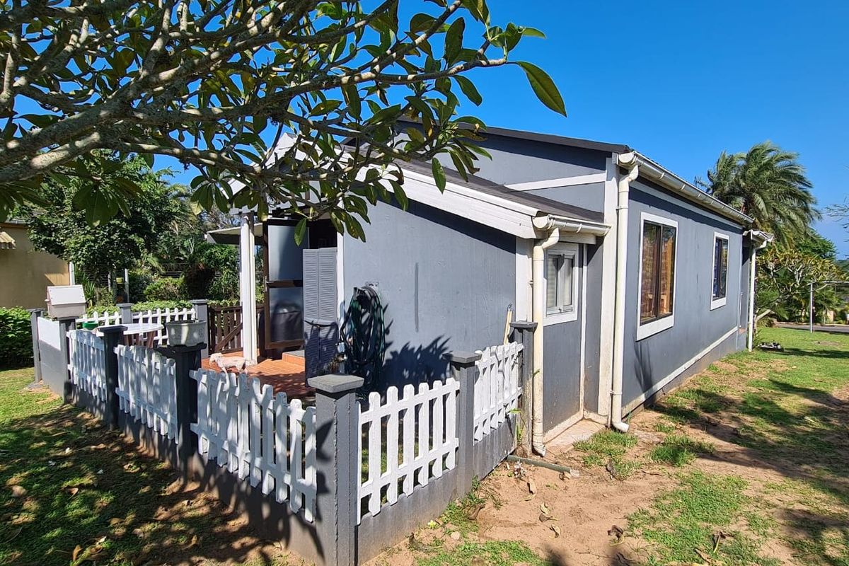 Rear view of the townhouse featuring a small tiled patio area enclosed by a white picket fence and established garden surroundings.