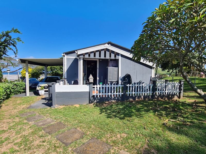Front exterior view of a detached townhouse featuring a carport, picket fencing, and a paved walkway set within a landscaped garden area.