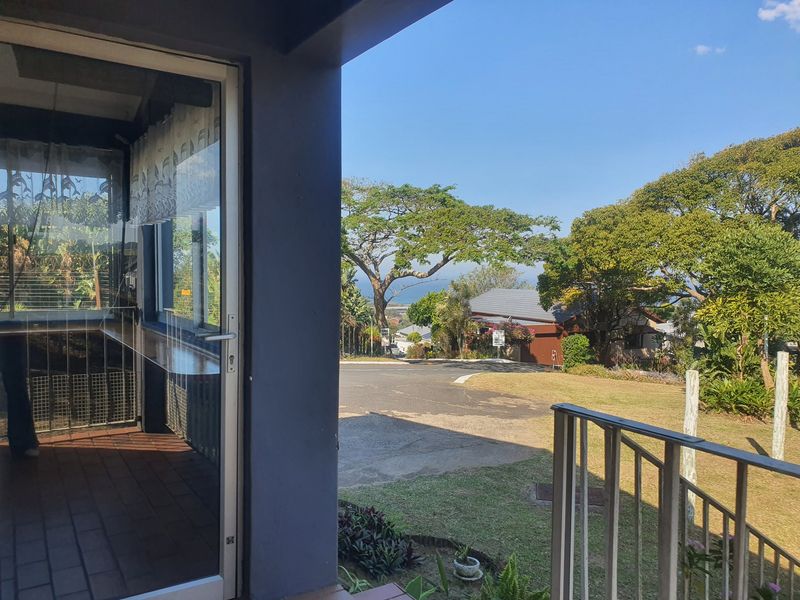 A covered patio area featuring tiled flooring and a sliding glass door, offering an open view of the surrounding neighborhood and garden.