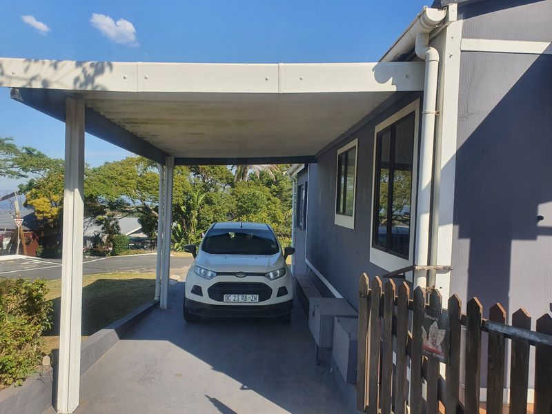 A covered carport area attached to the side of the townhouse, featuring a paved driveway and timber fencing.