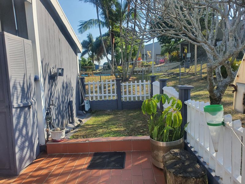 A rear patio area featuring terracotta tiling, a white picket fence, and a small grassed garden space.